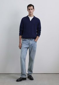 Suéter marino oscuro con diseño de cuello, combinado con jeans rectos de color azul claro y mocasines negros. Atuendo simple y casual.