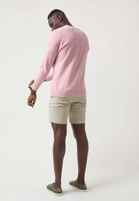 Suéter de punto color rosa claro con mangas largas, combinado con pantalones cortos caqui; usado con zapatos de lona verdes, mostrando texturas suaves y un diseño casual.