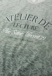 Tela de camuflaje verde claro con texto en blanco y negro que dice "ATELIER DE LECTURE Rue Saint-Vincent 72 UNIVERSITÉ DES PARIS."