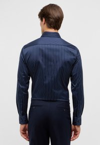 Camicia a righe blu navy con righe verticali bianche, polsini con bottoni e colletto classico. Tessuto morbido con un design aderente.