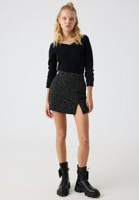 Jersey negro de punto con escote en V y mangas largas, combinado con una falda mini a cuadros en blanco y negro que cuenta con una abertura lateral y un tejido texturizado.