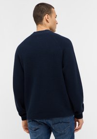 Dunkelblauer Pullover mit strukturiertem Strickdesign, geripptem Halsausschnitt und Ärmeln sowie einer lässigen Passform, kombiniert mit Jeans.
