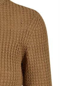 Gros plan sur l'épaule et le haut du bras d'un pull en maille marron texturé, avec un motif en point gaufré visible et des fibres douces et duveteuses.