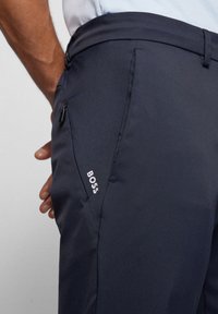 Navy trousers with a smooth texture, featuring a zip pocket and a white "BOSS" logo on the side. Tailored fit and classic design.