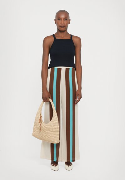 Black tank top, wide beige pants with brown and turquoise stripes, woven straw bag, and white shoes with a pointed toe detail.