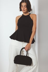 Juodas halter peplum topas su prigludusia liemenėle ir plačiu kraštu, derinamas su baltais plačiais kelniais. Laiko mažą juodą suknelę.