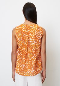 Top sin mangas con un patrón floral naranja sobre un fondo blanco, hecho de una tela ligera con una textura sutil y un corte relajado.