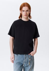 Zwarte korte mouwen T-shirt met een ronde hals, gemaakt van een gladde stof. Draagt een lichtblauwe distressed jeans met een sleutelhoezen detail.