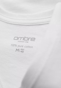 Bílá bavlněná tričko s označením "ombre bavlněná řada," "100 % čistá bavlna" a velikostními údaji "M" a "eur 48." Měkká textura.