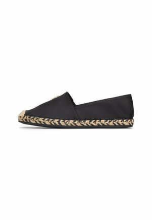 Espadrille en tissu noir avec une semelle en jute tissé. Dotée d'un bout arrondi et d'un petit accent métallique sur le côté. Design plat, sans talon.
