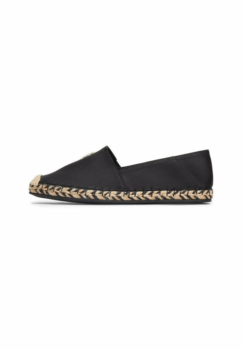 Espadrille en tissu noir avec une semelle en jute tissé. Dotée d'un bout arrondi et d'un petit accent métallique sur le côté. Design plat, sans talon.