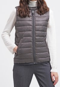Gilet grigio puffoso con collo alto, chiusura con zip e due tasche frontali; presenta un motivo a quadrati orizzontali e un tessuto dalla superficie liscia.