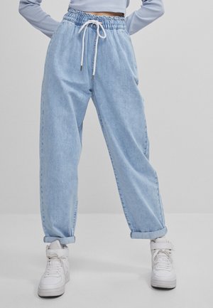 Person wearing light blue loose-fit denim pants with a drawstring waist and rolled cuffs, paired with white high-top sneakers.