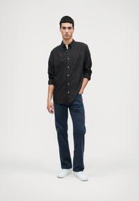 Fekete kockás ing, gombos kialakítással, sötétkék kordbársony nadrággal és fehér sportcipővel párosítva. A modell egyszínű háttér előtt áll.