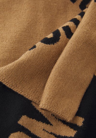 Strikkegenser med leopardmønster i svart på en beige bakgrunn. Myk tekstur med brettet kant som viser vevd detalj.