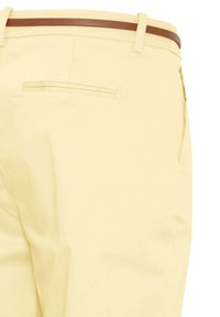 Pantalon beige avec une ceinture marron, doté d'une poche passepoilée arrière et d'une couture latérale visible.