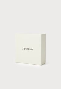 Boîte rectangulaire blanche avec une finition lisse, arborant le logo "Calvin Klein" en texte sombre subtil à l'avant. Design minimaliste.