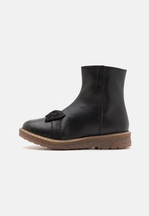 Zwarte leren enkellaars met een afgeronde neus, voorzien van een gestructureerde strik aan de voorkant en een bruine rubberen zool.