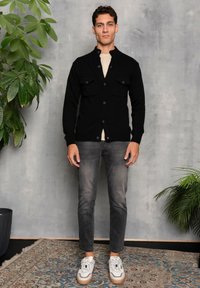 Black wool blend cardigan with two front pockets, paired with light-colored T-shirt, gray jeans, and white sneakers with brown accents.