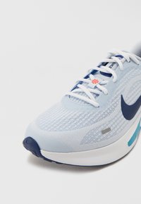 Light blue athletic shoe featuring a textured mesh upper, white laces, navy accents, and a cushioned sole with orange branding detail.