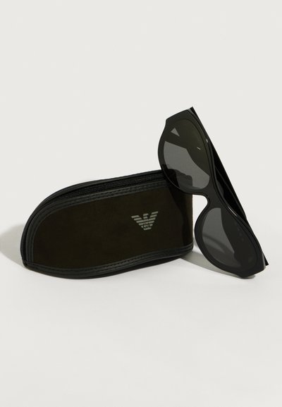 Čierne slnečné okuliare s elegantným, uhlovým dizajnom a tmavými šošovkami, ležiace na čiernom uzáverovom puzdre s logom vyrazeným na prednej strane.