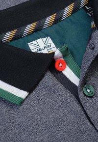 Grijze poloshirt met een textuurstof, zwarte kraag met groene, witte en gele strepen, en twee contrasterende knoopaccenten.