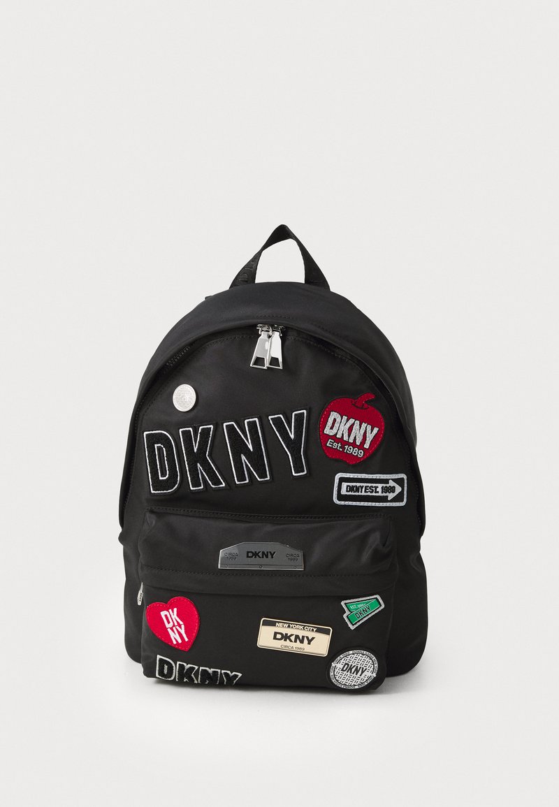 Black fabric backpack featuring multiple patches, zippers, and a handle. Notable patches include "DKNY" and various logos. Compact design.