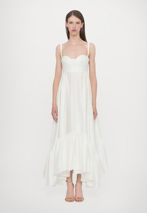 Witte jurk met een getailleerde corsage, dunne bandjes en een vloeiende, gelaagde rok. Glad materiaal, asymmetrische zoom en minimalistisch ontwerp.