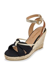 Wedge sandal featuring a black fabric upper with a knot detail, gold ankle strap, and a textured jute-wrapped heel.