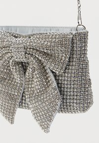 Srebrna torebka kopertówka ozdobiona błyszczącymi cyrkoniami, z dużą kokardą, miękką podszewką wewnętrzną i odpinanym łańcuszkiem.