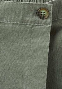 Tessuto di velluto a coste verde con righe verticali, con chiusura a bottone in vita. La texture è morbida e leggermente a coste.