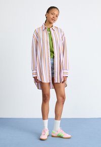 Koszula na guziki w paski w kolorze lawendowym, żółtym i jasnoniebieskim; zestawiona z zielonym t-shirtem i dżinsowymi szortami. Noszona z różowymi butami i białymi skarpetkami.