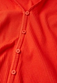 Red ribbed fabric with a button-up design. Six round buttons in matching color running vertically. Soft texture with slight draping.