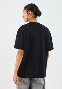 T-shirt noir à manches courtes avec col rond, fabriqué en coton doux. Coupe décontractée avec des épaules tombantes. Texture lisse, minimalisme des détails.