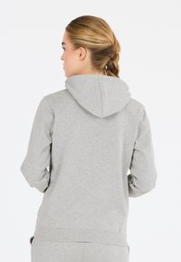 Jasnoszara bawełniana bluza z kapturem, z sznurkiem do regulacji, prążkowanymi mankietami i dołem. Charakteryzuje się gładką fakturą i luźnym krojem. Widok z tyłu.