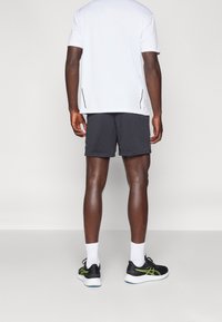 Herrkläder för sport med en kortärmad vit skjorta och mörkgrå shorts. Egenskaper inkluderar en lös passform, andningsbart tyg och svarta löparskor med gröna detaljer.