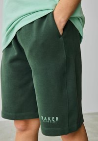 Zaļi kokvilnas šorti ar sānu kabatām un ribotām malām. Uz apakšējās kājas ir balts "BAKER by TED BAKER" logo.