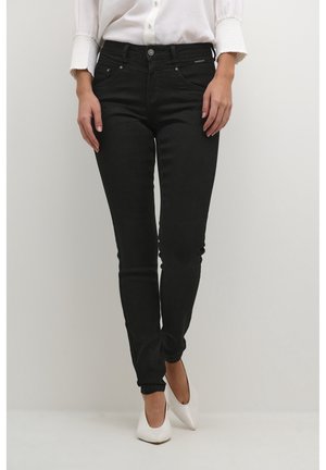 Pantalones vaqueros ajustados negros con una textura suave, diseño de cinco bolsillos y cierre de botón metálico. Combinados con una blusa blanca y tacones blancos.