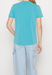 T-shirt turchese a maniche corte con vestibilità rilassata, colletto rotondo e maniche arrotolate, abbinato a pantaloni cargo azzurri chiari con tasche.