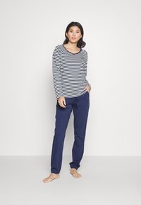 Lange mouwen, marineblauw en wit gestreepte top met ronde hals, gecombineerd met effen marineblauwe broek met elastische manchetten en zakken.