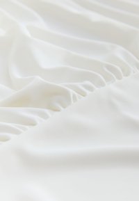 White fabric with a smooth texture, featuring gathered ruffles along one edge. The material appears lightweight and soft.