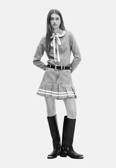 Een denimhemd met een witte kraag en strikjes, gecombineerd met een uitlopende denimrok met witte strepen. Zwarte kniehoog laarzen met gespen.