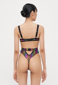 Bikini à motif serpent multicolore brillant avec des bretelles noires ; présente un design à haute coupe et des fermetures ajustables au dos.