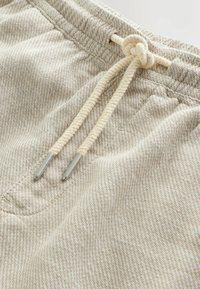 Pantaloni in tessuto beige dalla trama strutturata con vita elastica e coulisse color crema annodata a fiocco con terminali metallici vicino alla tasca frontale.