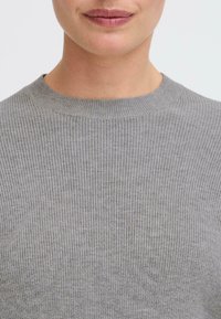 Grauer Strickpullover mit gerippter Textur und Rundhalsausschnitt, der eine glatte, weiche Oberfläche aufweist. Nahaufnahme des oberen Stoffdetails.