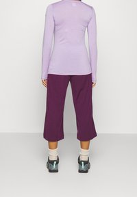 Ljuslila långärmad tröja, tillsammans med cropped lila byxor. Bär svarta och teal skor med vita strumpor. Enkel, bekväm sportklädsel.