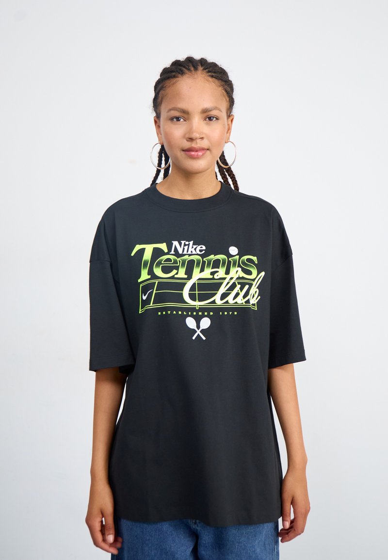 Juodas per didelis marškinėliai, pagaminti iš medvilnės, su neoninės žalios spalvos "Nike Tennis Club" grafika, kurioje yra teniso motyvų ir įkūrimo data.