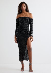 Zwarte off-the-shoulder pailletten jurk met lange mouwen en hoge split tot boven de dij. Heeft een gerimpeld ontwerp en een gladde, reflecterende textuur.