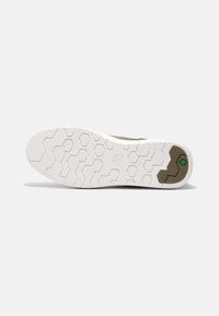 A sola do tênis apresenta uma base de borracha branca com um padrão de ranhura hexagonal e um acabamento verde escuro perto do calcanhar. Textura lisa no geral.