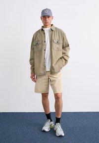 Light beige denim shirt over a white t-shirt, paired with light shorts. A striped cap, black socks, and silver sneakers complete the look.